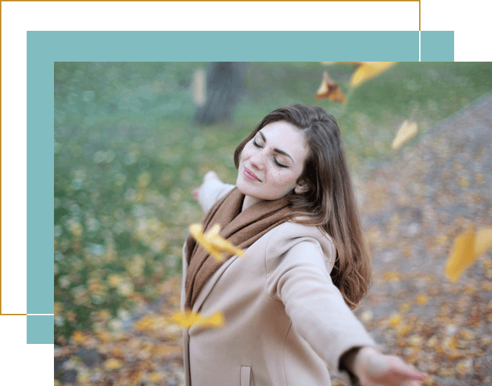 A woman in the park throwing leaves into the air.