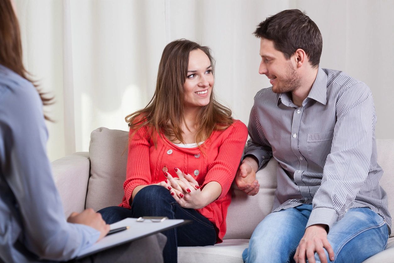 A man and woman sitting on the couch talking to each other.